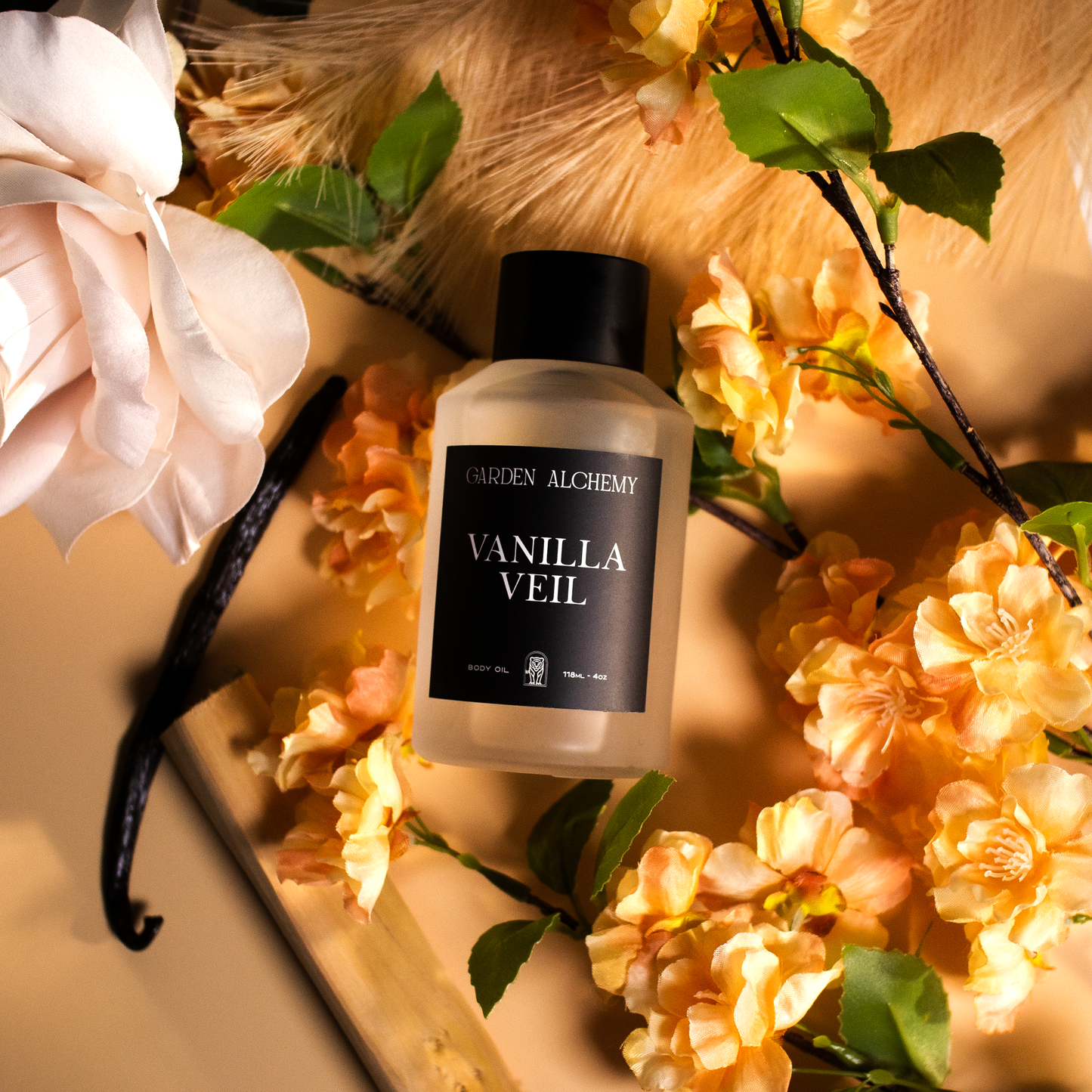 A bottle of GARDEN ALCHEMY VANILLA VEIL PERFUME BODY OIL is elegantly displayed on a beige surface, surrounded by peach flowers, a white rose, pale beige leaves, and a vanilla bean.